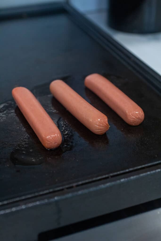 Cooking the hot dogs on a griddle or pan.
