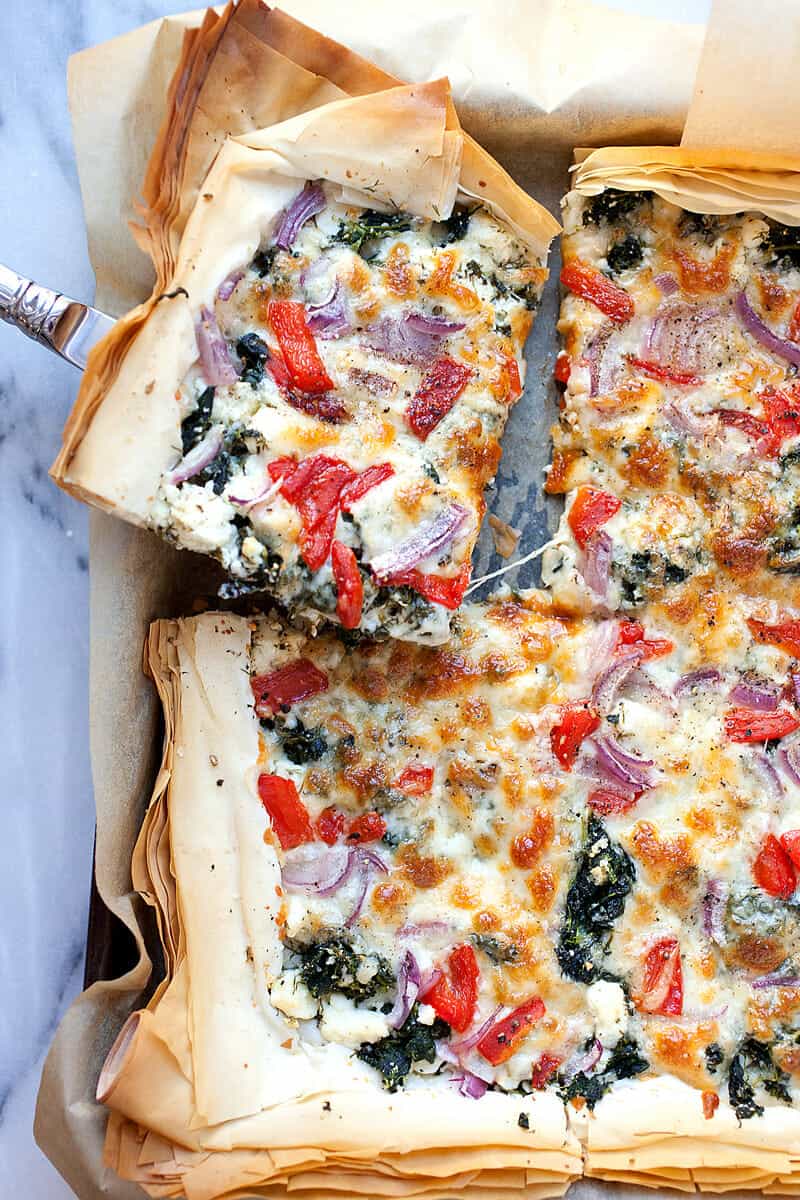 Spanakopizza: A perfect mash-up between flaky spanakopita and a delicious pizza. Loaded with spinach, feta, and roasted red peppers, but it still has a flaky phyllo dough crust! Great for a meal or appetizer. | macheesmo.com