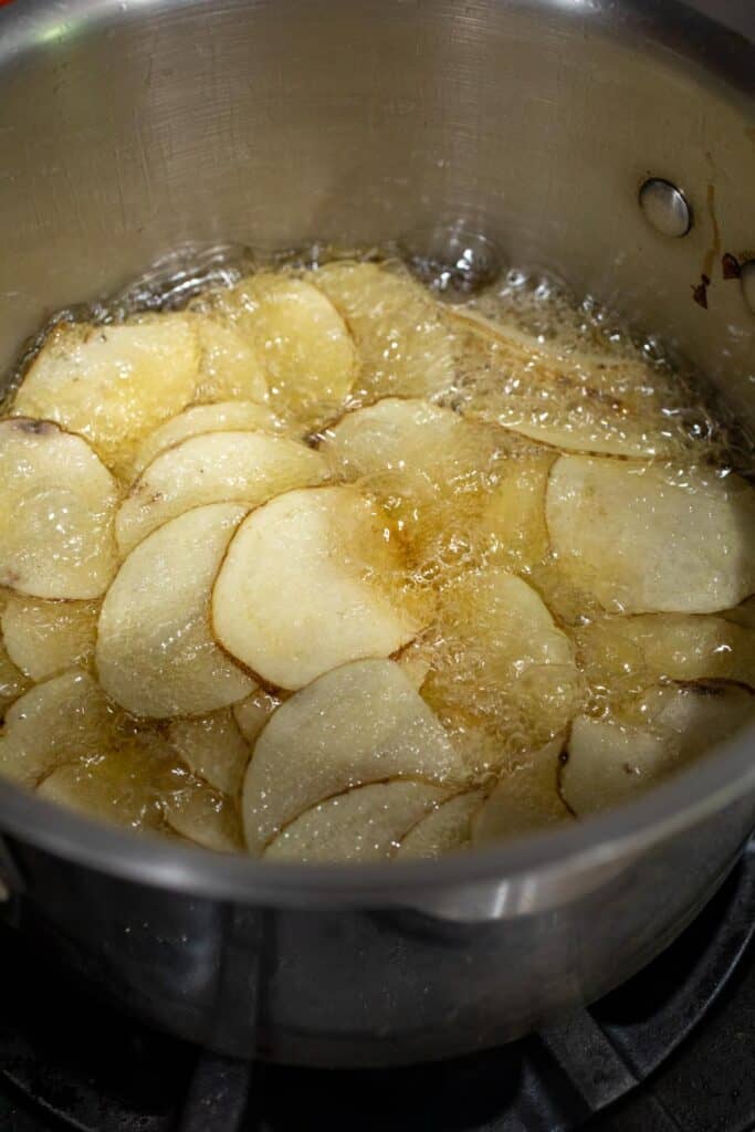 Chips frying in hot oil in a pot.