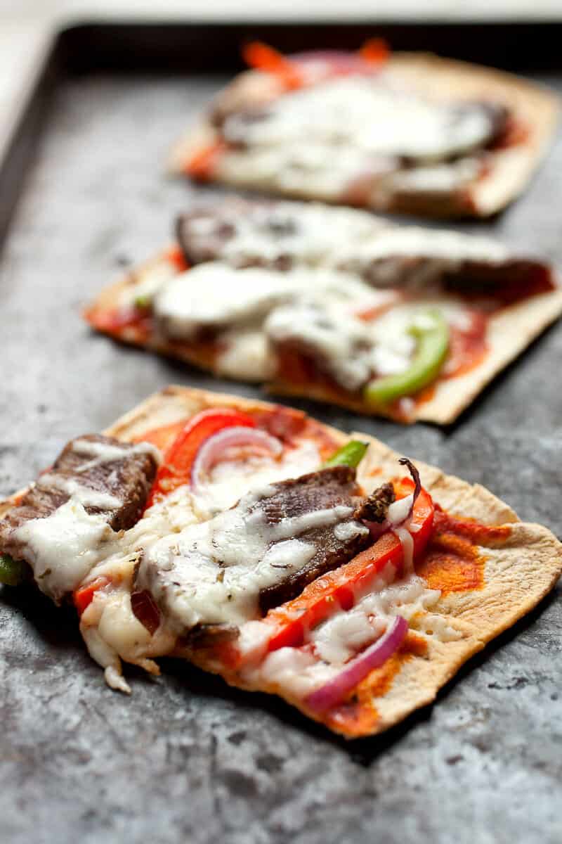 Cheesesteak Flatbread: Flatbreads topped with sliced sirloin steak, peppers, onions, and provolone cheese. Great as a meal or a hearty appetizer. Super easy to make thanks to Flatout Flatbread pizza crust! #sponsored | macheesmo.com