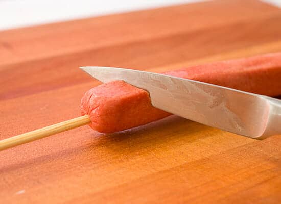 Cutting the spiral hot dog with a skewer.