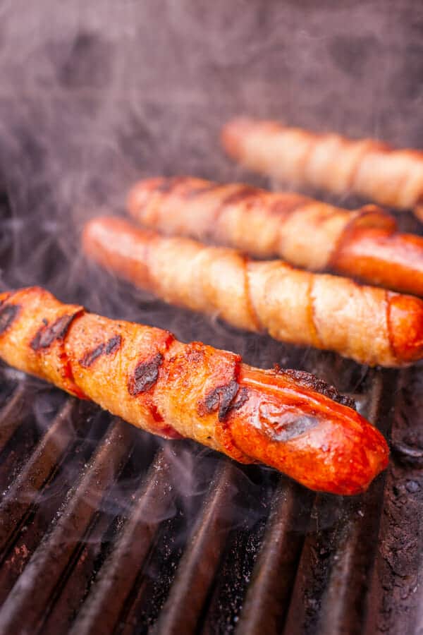 Grilling hot dogs with bacon wrapping.