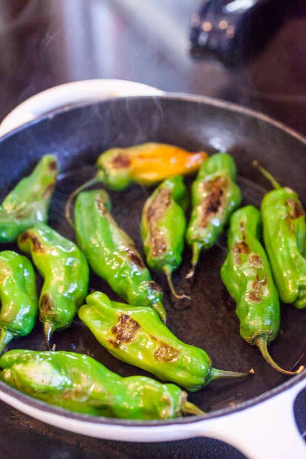 Charred shishito peppers in a skillet.