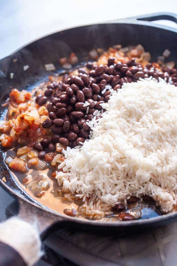 Adding beans to the skillet for the cheesy beans and rice.