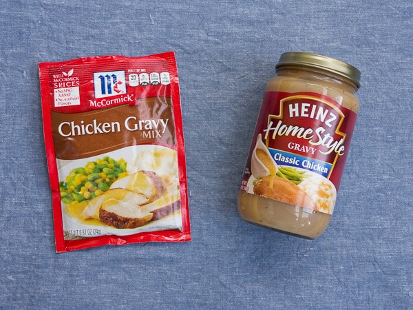 A package of powdered gravy mix next to a jar of premade gravy on a blue background
