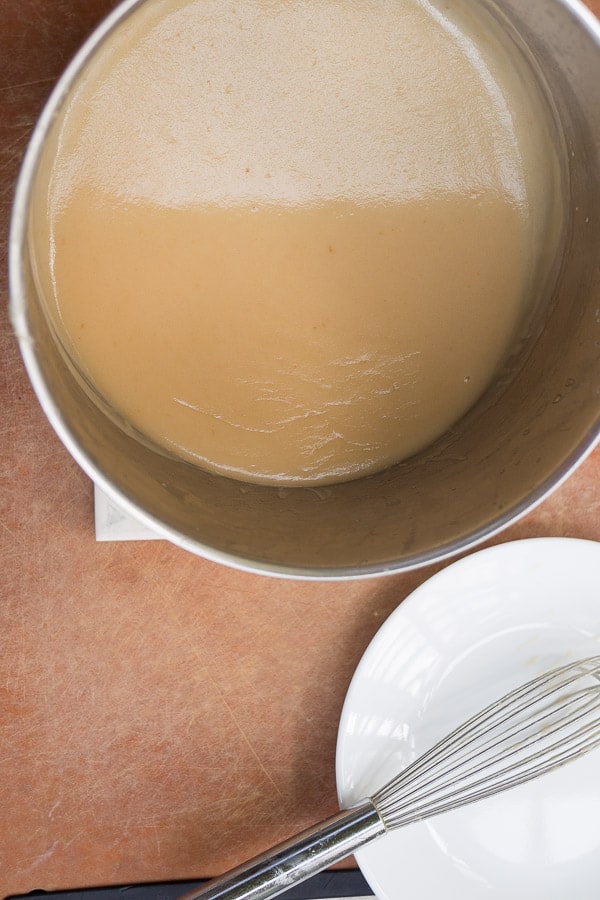 thickened gravy in saucepan next to a whisk and plate 