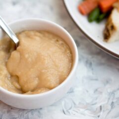 homemade gravy in white bowl next to a plate of chicken