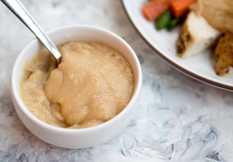 homemade gravy in white bowl next to a plate of chicken