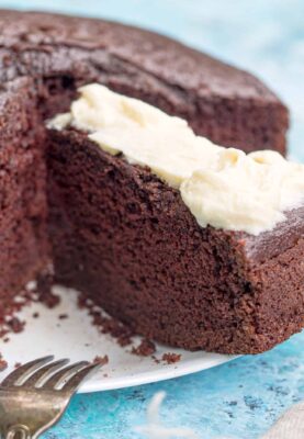 homemade chocolate cake on a white plate with cream cheese frosting