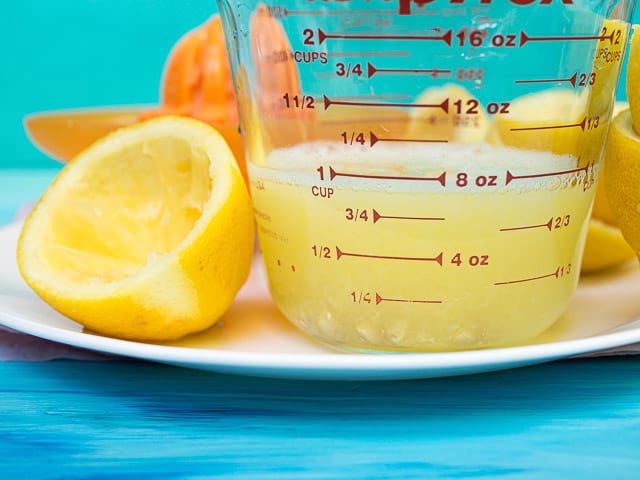 A cup of lemon juice in a glass measuring cup next to lemon halves