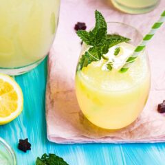 A glass of lemonade with a mint garnish and a green-white striped straw