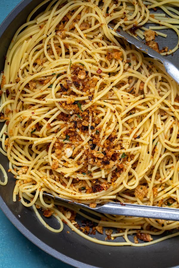 Mixing in breadcrumbs into cooked spaghetti.