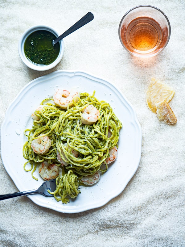 A plate of pasta and shrimp tossed in pesto next to more pesto and cheese.