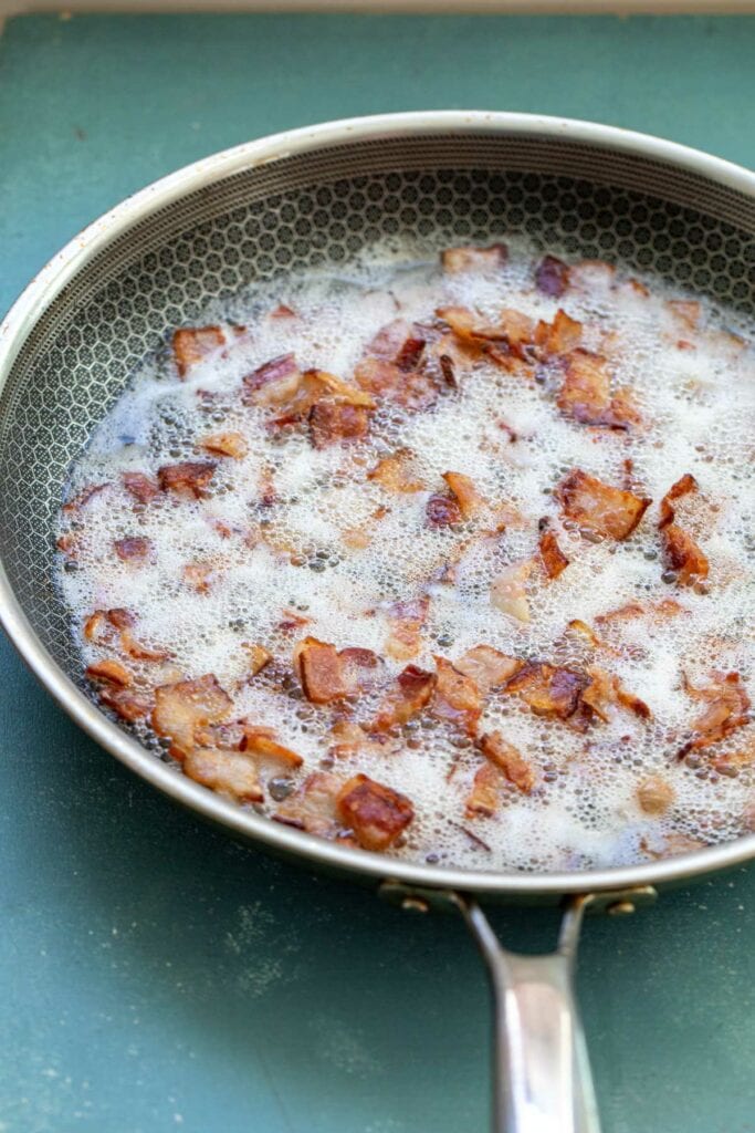 Bacon bits cooking in a skillet. 