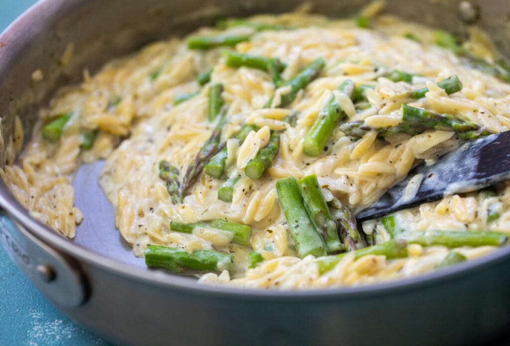 Creamy orzo with asparagus in a skillet.